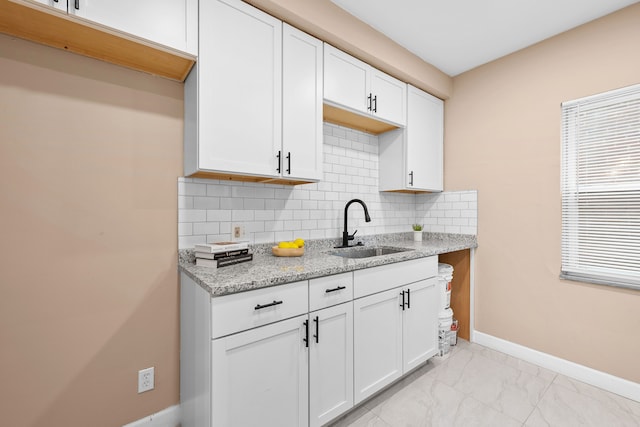 kitchen with a wealth of natural light, sink, tasteful backsplash, light stone counters, and white cabinets