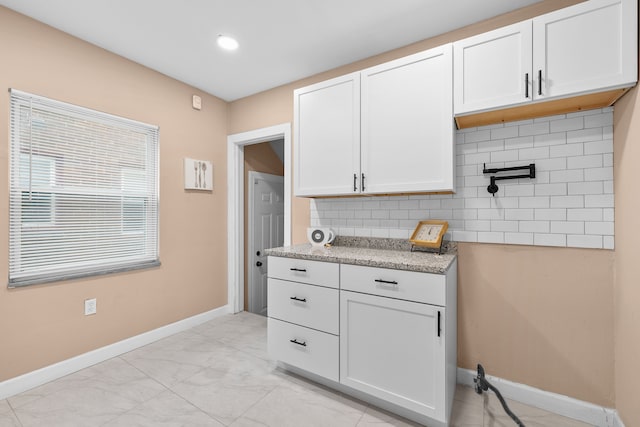 kitchen featuring white cabinets, light stone countertops, and backsplash