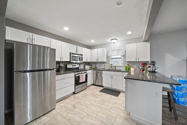kitchen with dark stone countertops, a sink, a peninsula, appliances with stainless steel finishes, and white cabinetry