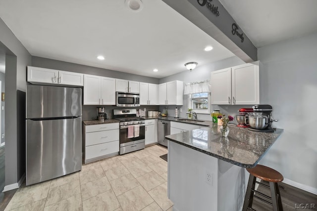 kitchen featuring white cabinets, stainless steel appliances, a peninsula, dark stone countertops, and recessed lighting