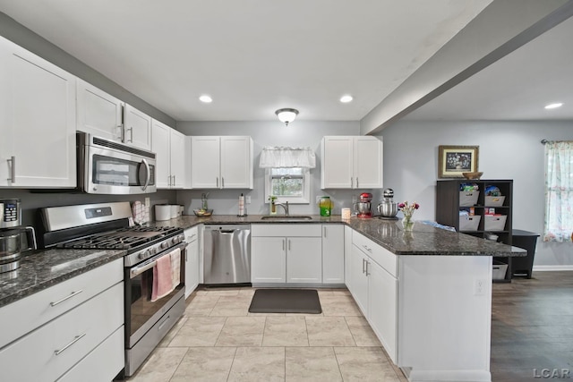 kitchen with white cabinets, a peninsula, stainless steel appliances, and a sink