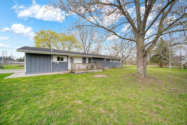 rear view of house with board and batten siding, a lawn, and a deck