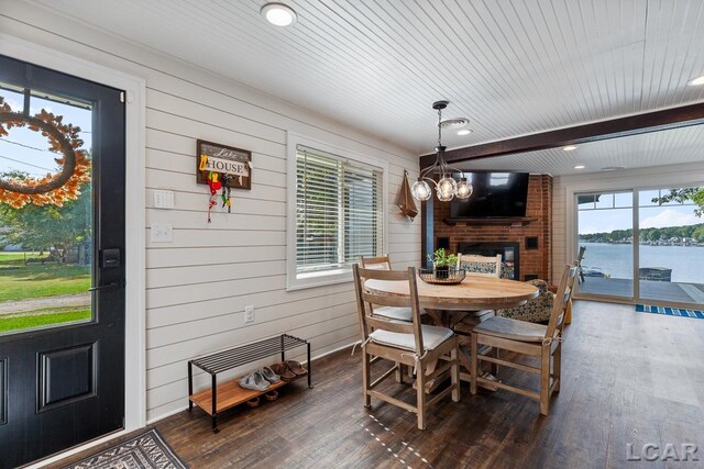 dining room featuring a brick fireplace, dark hardwood / wood-style floors, wood walls, and an inviting chandelier