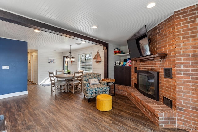 living room featuring beam ceiling, dark wood-type flooring, a notable chandelier, and a brick fireplace