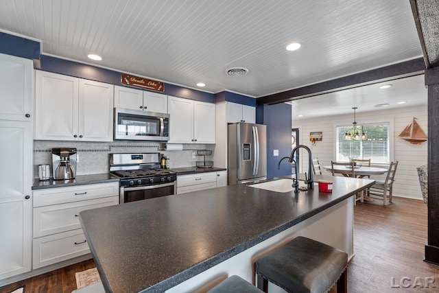 kitchen featuring hanging light fixtures, stainless steel appliances, wood-type flooring, a kitchen bar, and white cabinets