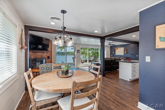 dining room with ceiling fan with notable chandelier, sink, a fireplace, dark hardwood / wood-style flooring, and brick wall