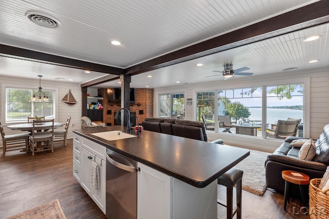 kitchen with a wood stove, white cabinetry, sink, stainless steel dishwasher, and a kitchen island with sink