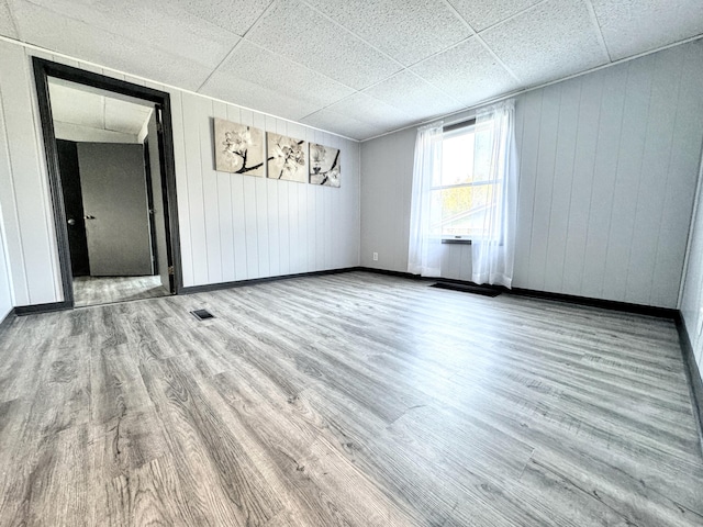 empty room with a paneled ceiling, hardwood / wood-style flooring, and wood walls