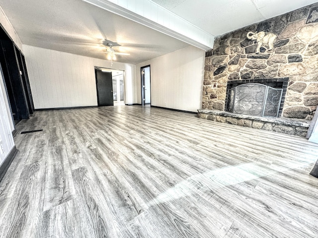 unfurnished living room featuring a textured ceiling, ceiling fan, beamed ceiling, a fireplace, and hardwood / wood-style floors