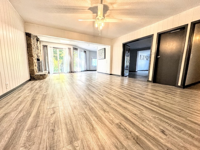 spare room with ceiling fan, light hardwood / wood-style floors, a stone fireplace, and a textured ceiling