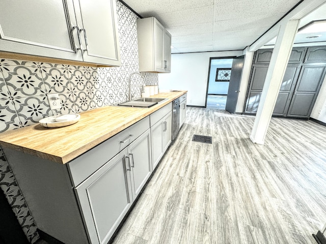 kitchen with wood counters, sink, light hardwood / wood-style flooring, stainless steel dishwasher, and gray cabinets