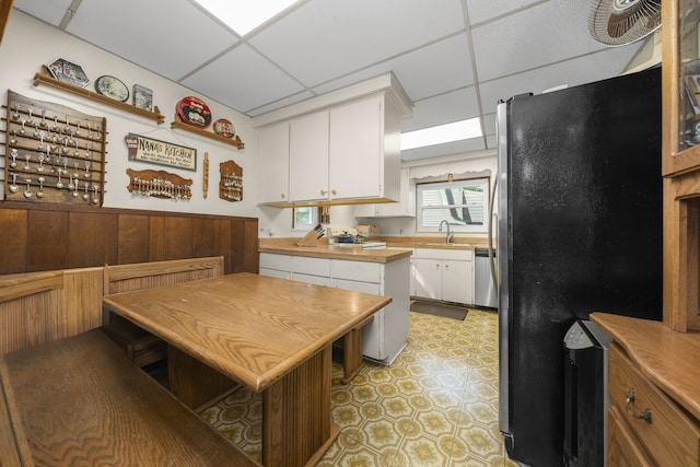 kitchen featuring dishwasher, black fridge, wood walls, a paneled ceiling, and white cabinets