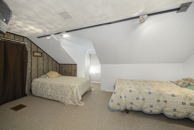 carpeted bedroom with a textured ceiling, lofted ceiling, and wood walls