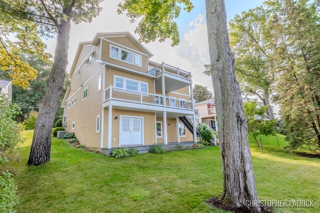 rear view of property with a lawn, board and batten siding, central AC, a balcony, and stairs