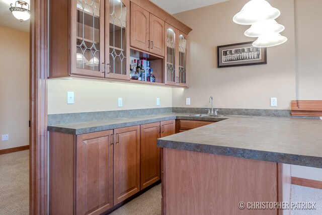 kitchen featuring dark countertops, a peninsula, glass insert cabinets, and a sink