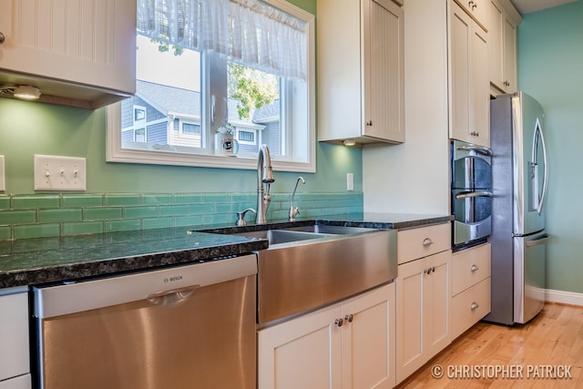 kitchen with stainless steel appliances, light wood finished floors, dark stone countertops, and a sink