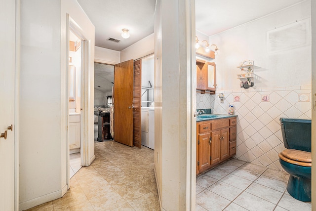 bathroom featuring vanity, tile patterned floors, toilet, tile walls, and washer / clothes dryer