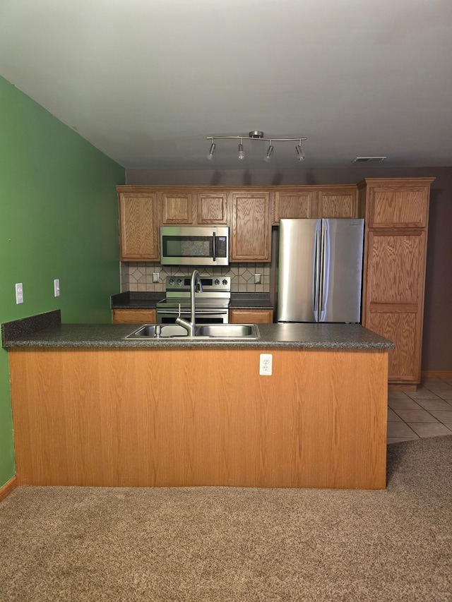 kitchen featuring decorative backsplash, kitchen peninsula, stainless steel appliances, sink, and tile patterned flooring