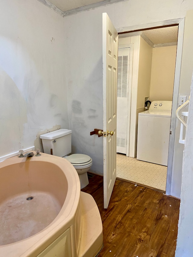 bathroom with ornamental molding, hardwood / wood-style flooring, washer / dryer, toilet, and a bathing tub