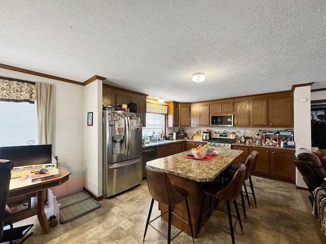 kitchen with a kitchen bar, appliances with stainless steel finishes, ornamental molding, a textured ceiling, and a center island