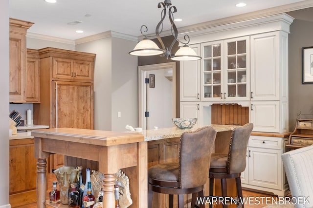 interior space with crown molding, hardwood / wood-style floors, pendant lighting, and light stone counters