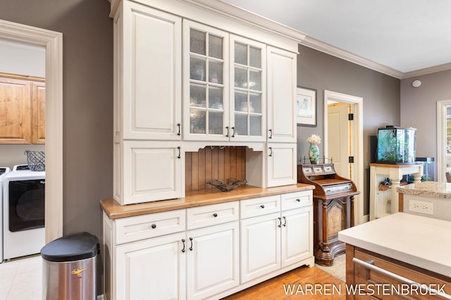 kitchen with light hardwood / wood-style floors, white cabinetry, ornamental molding, and washing machine and clothes dryer