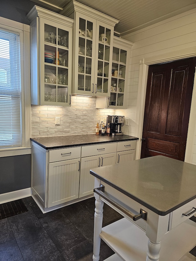 kitchen featuring wood walls, dark tile patterned flooring, decorative backsplash, ornamental molding, and white cabinetry