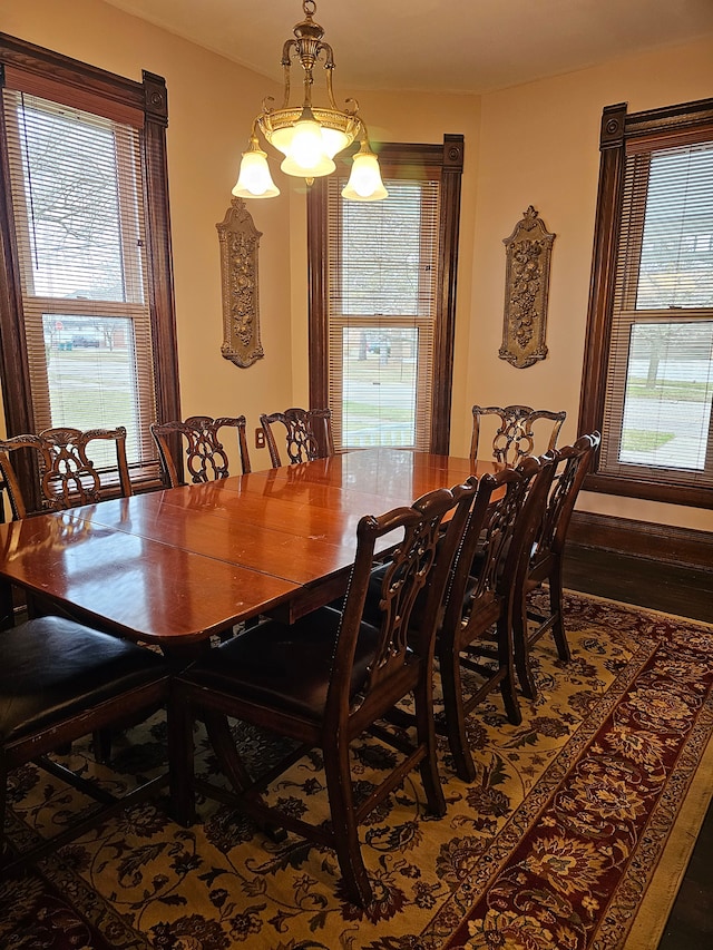 dining room with dark wood-type flooring, a healthy amount of sunlight, and an inviting chandelier