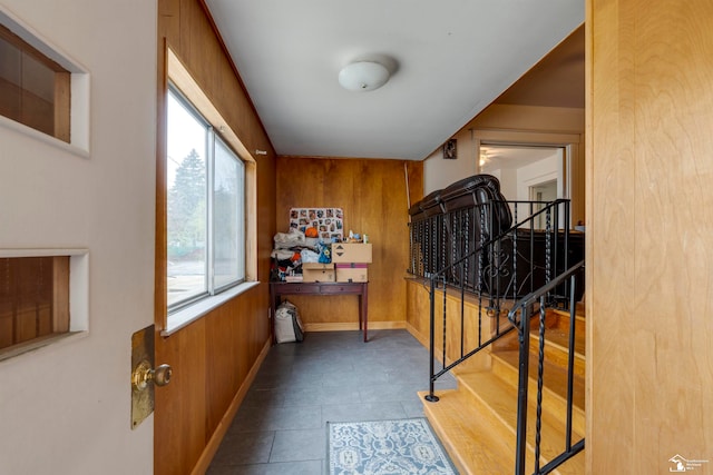 hallway with dark tile patterned flooring, plenty of natural light, and wood walls