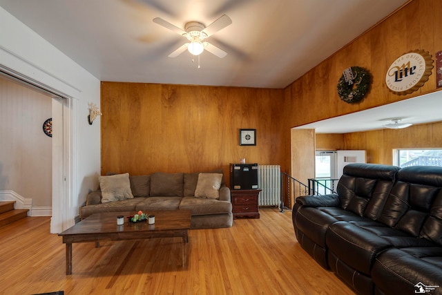 living room with ceiling fan, light hardwood / wood-style flooring, wood walls, and radiator heating unit