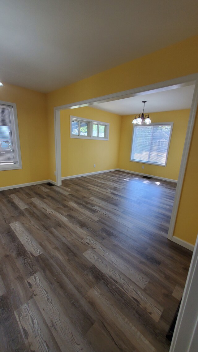 empty room featuring a chandelier, dark wood-style floors, and baseboards