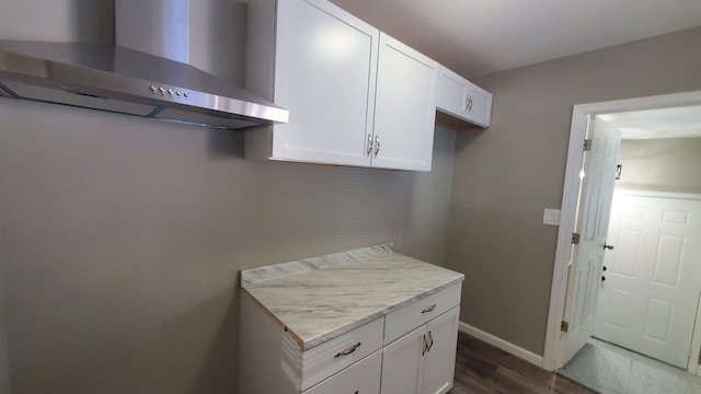 kitchen with light stone countertops, white cabinets, dark hardwood / wood-style floors, and wall chimney range hood