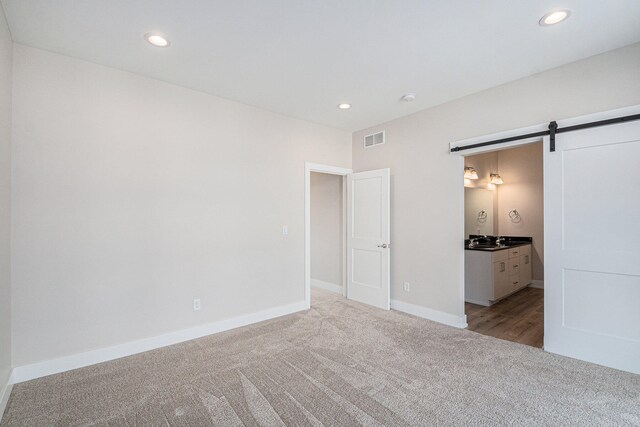 unfurnished bedroom featuring a barn door, light carpet, and connected bathroom