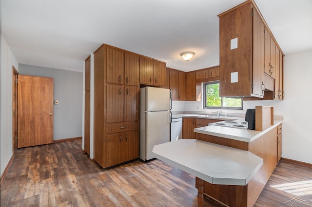 kitchen featuring sink, a kitchen breakfast bar, dark hardwood / wood-style flooring, kitchen peninsula, and white appliances