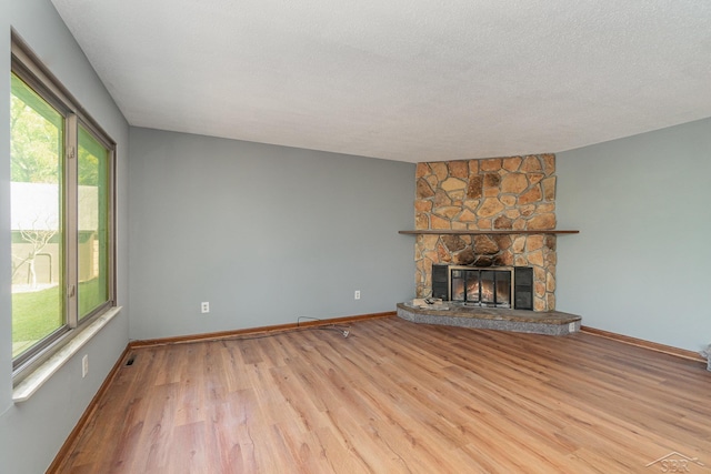 unfurnished living room with a stone fireplace, a textured ceiling, and light wood-type flooring