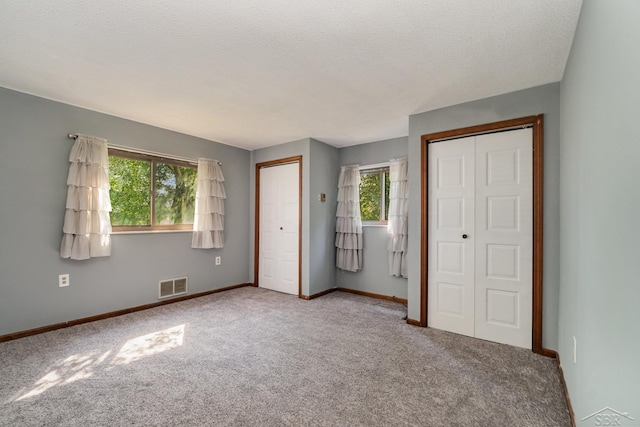 unfurnished bedroom with a textured ceiling, carpet floors, and multiple windows