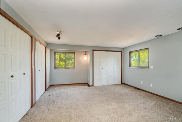 unfurnished bedroom with multiple windows, multiple closets, light colored carpet, and a textured ceiling