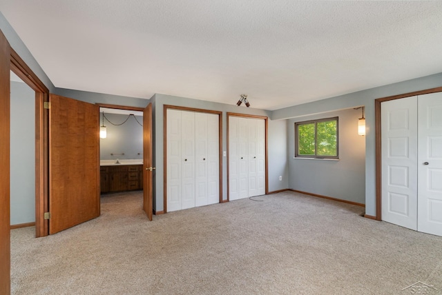 unfurnished bedroom with a textured ceiling, ensuite bathroom, light carpet, and two closets