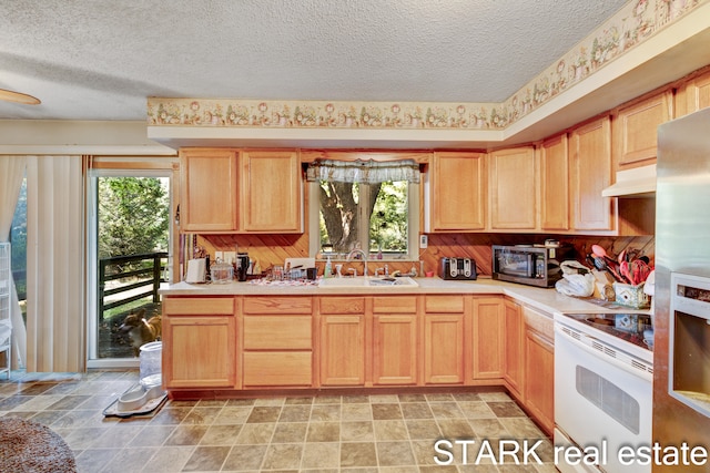 kitchen with light brown cabinetry, sink, stainless steel appliances, and a textured ceiling