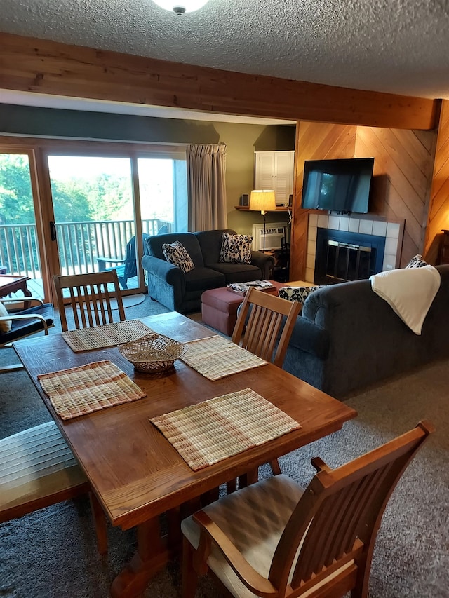 carpeted dining room with a fireplace, a textured ceiling, beamed ceiling, and wood walls