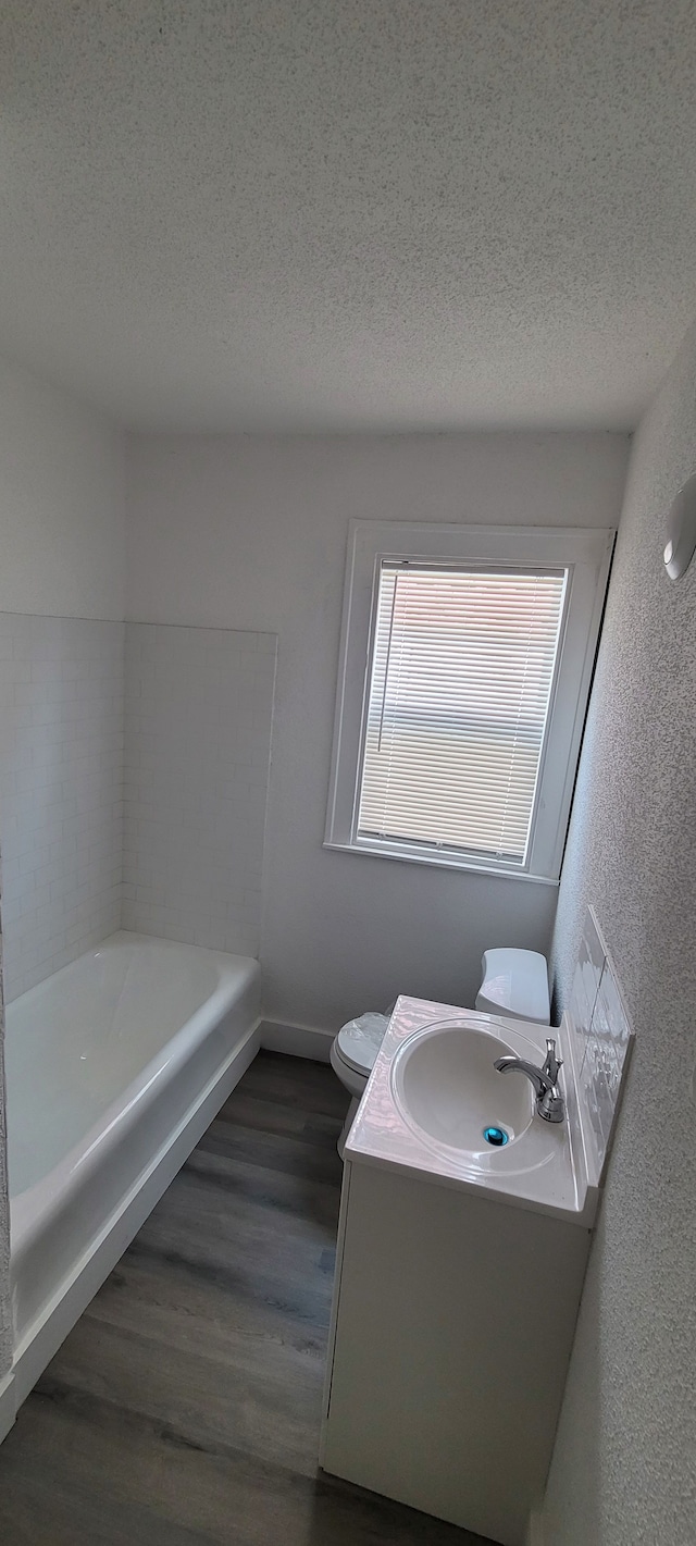 bathroom with hardwood / wood-style flooring, a washtub, toilet, and a textured ceiling