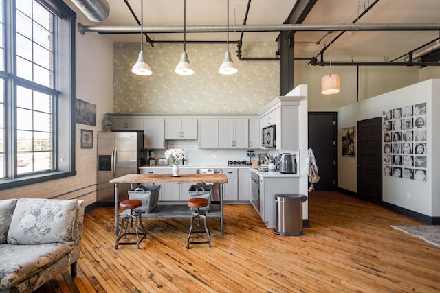 kitchen featuring a towering ceiling, hanging light fixtures, and appliances with stainless steel finishes