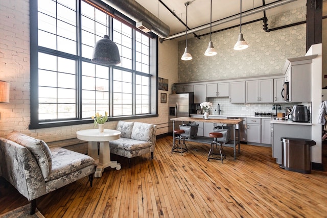 kitchen featuring wallpapered walls, a high ceiling, gray cabinets, appliances with stainless steel finishes, and hardwood / wood-style flooring