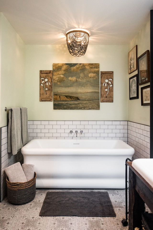 full bath with tile walls, a soaking tub, a notable chandelier, and wainscoting