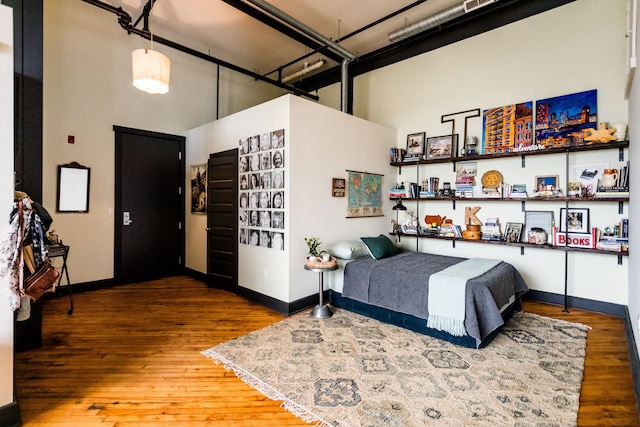 bedroom featuring baseboards, wood finished floors, and a high ceiling