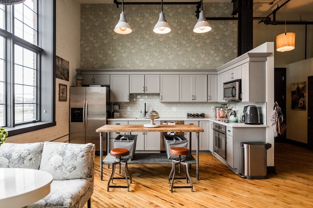kitchen with a high ceiling, stainless steel appliances, wallpapered walls, and light wood-style flooring