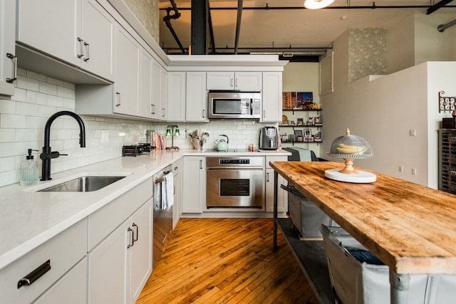 kitchen featuring a sink, wood counters, decorative backsplash, light wood-type flooring, and appliances with stainless steel finishes