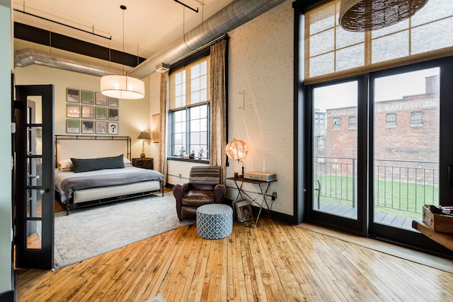 bedroom featuring hardwood / wood-style floors, brick wall, a towering ceiling, and access to outside