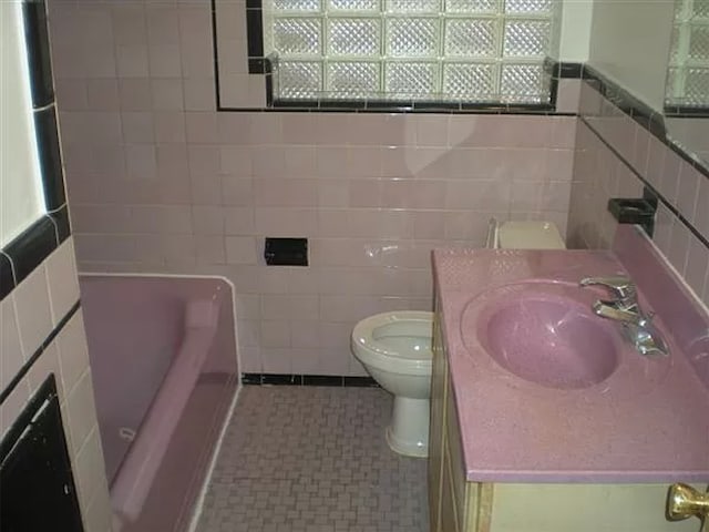 bathroom with a bathtub, vanity, tile walls, and toilet