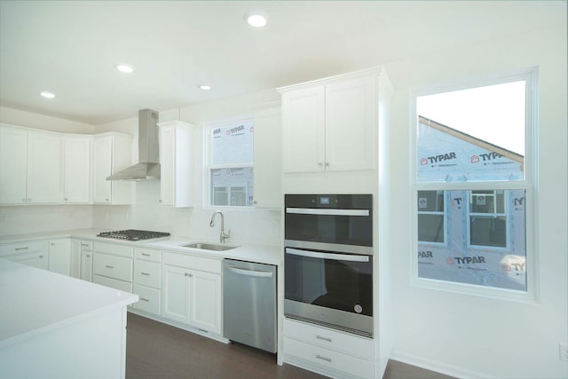 kitchen featuring white cabinetry, wall chimney range hood, sink, and appliances with stainless steel finishes